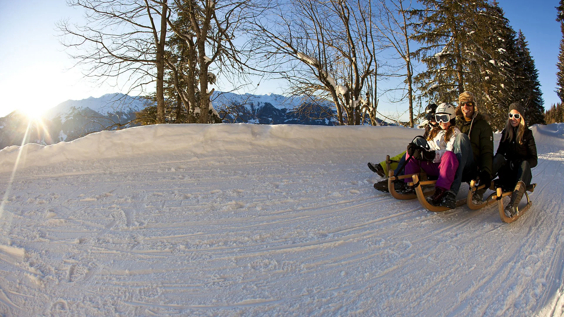 Four people sledding happily on a snowy winter track with sunshine