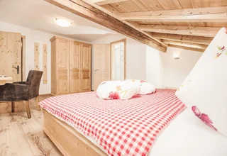 Cozy bedroom with wooden furniture and red checkered bedding under slanted wooden ceiling