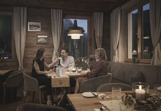 Three people drinking wine and chatting in a cozy wooden-decorated restaurant.