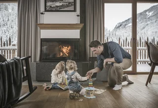 Father playing with two children near fireplace in cozy room with snowy mountain view