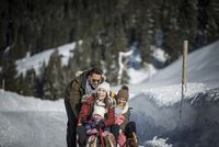 Familie beim Schlittenfahren auf verschneitem Weg im Winterwald