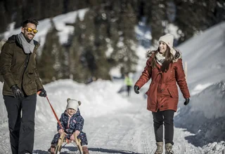 Family with small child sledding on snow while walking outdoors