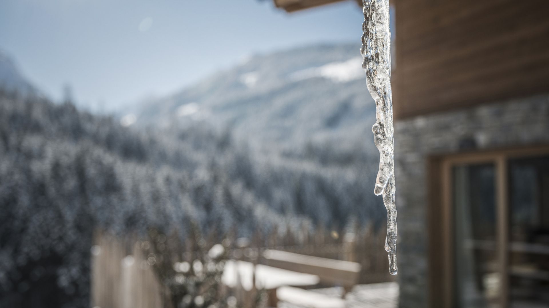 Ein Eiszapfen hängt an einer Hütte vor verschneiten Bergen