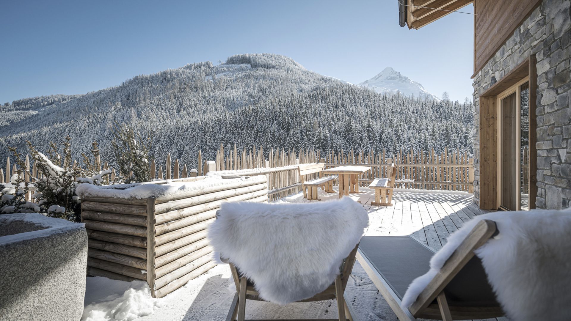 Farm Resort Geislerhof Winter terrace with wooden chairs and view of snowy mountains and forest