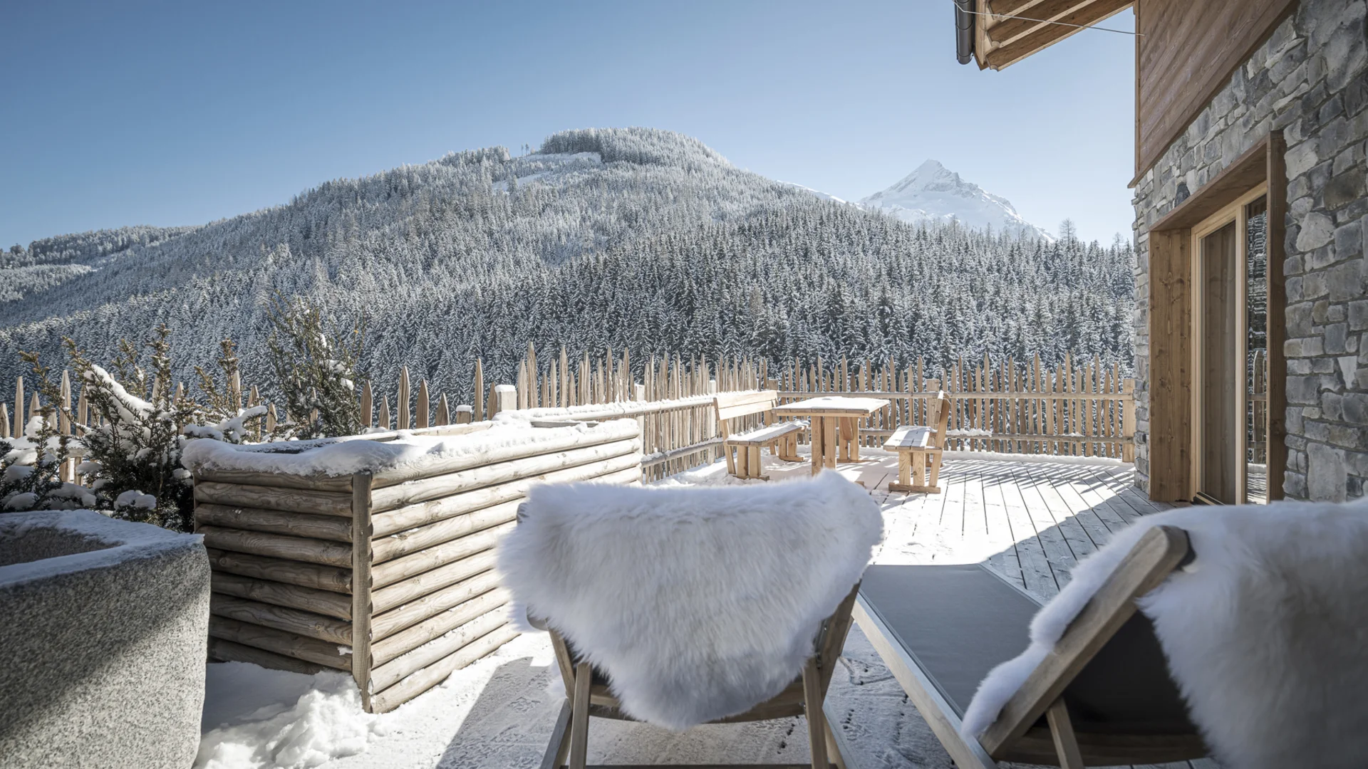 Winterterrasse mit Holzstühlen und Blick auf verschneite Berge und Wald